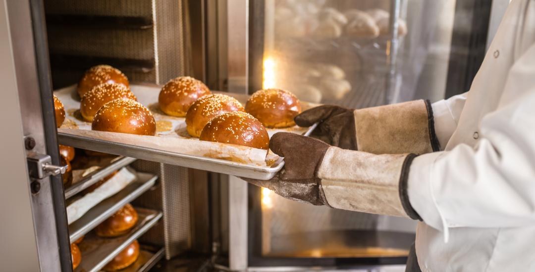 Bäcker holt Brötchen aus dem Ofen.